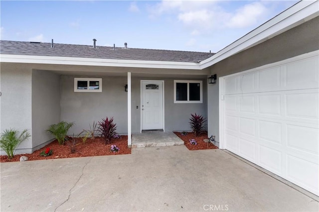 view of exterior entry featuring roof with shingles, an attached garage, and stucco siding