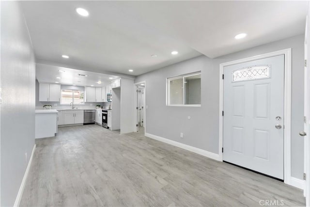 unfurnished living room featuring recessed lighting, light wood-type flooring, a sink, and baseboards