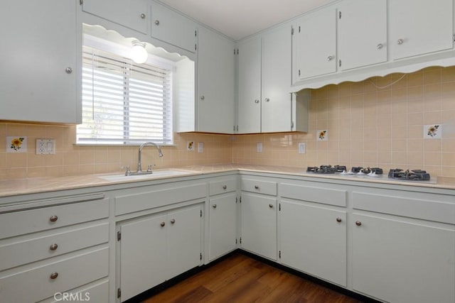 kitchen with white gas stovetop, a sink, light countertops, backsplash, and dark wood-style floors