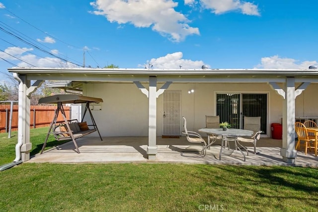 rear view of house with stucco siding, fence, a lawn, and a patio