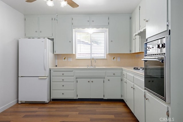 kitchen with a sink, black oven, backsplash, freestanding refrigerator, and dark wood finished floors