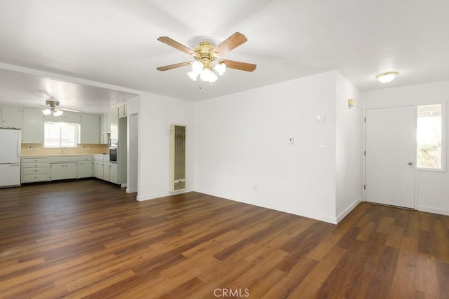 unfurnished living room featuring dark wood-style floors, a sink, a ceiling fan, and baseboards