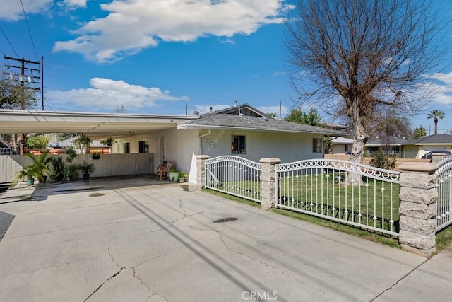 view of front facade with concrete driveway, a fenced front yard, an attached carport, a gate, and stucco siding