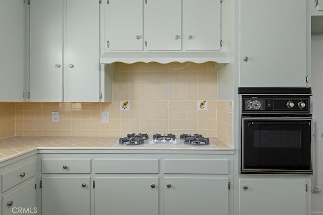 kitchen with tile countertops, decorative backsplash, white gas cooktop, white cabinetry, and oven