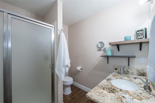 bathroom with toilet, wood finished floors, vanity, baseboards, and a stall shower