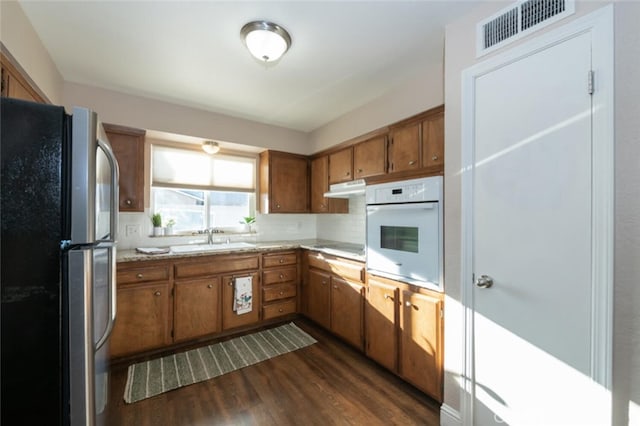 kitchen featuring visible vents, brown cabinetry, white oven, freestanding refrigerator, and a sink