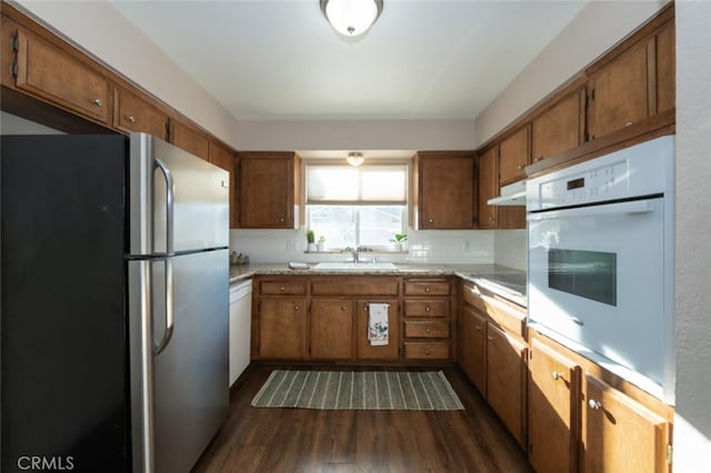 kitchen featuring white appliances, brown cabinetry, dark wood-style flooring, light countertops, and a sink