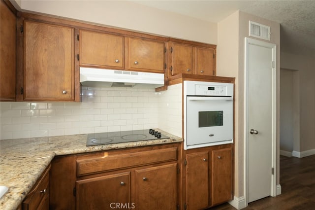 kitchen featuring brown cabinets, black electric stovetop, visible vents, oven, and under cabinet range hood