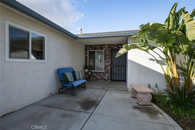 doorway to property with a patio area, brick siding, and stucco siding