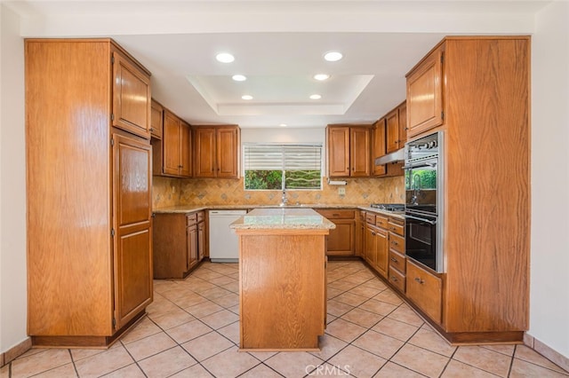 kitchen featuring a tray ceiling, tasteful backsplash, dobule oven black, a kitchen island, and white dishwasher