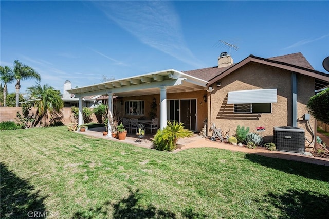 back of property with a yard, a chimney, a patio, stucco siding, and central AC