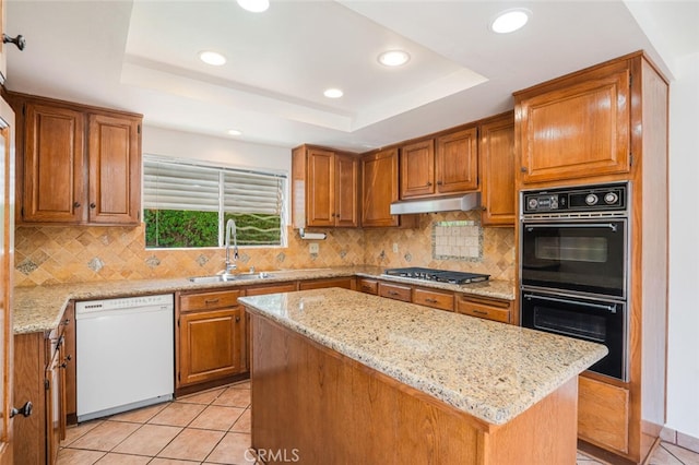 kitchen featuring a raised ceiling, dobule oven black, white dishwasher, a sink, and under cabinet range hood