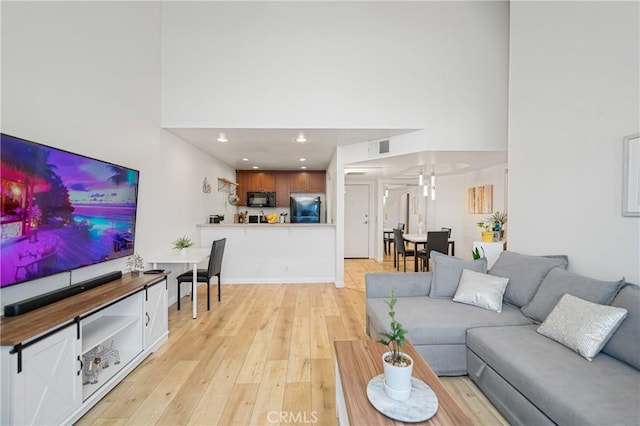 living area featuring visible vents, light wood finished floors, a towering ceiling, and recessed lighting