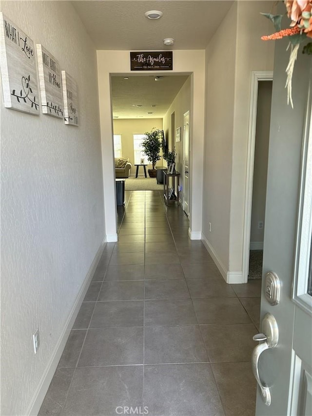 hall with dark tile patterned floors and baseboards