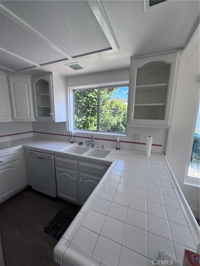 kitchen featuring glass insert cabinets, white dishwasher, tile counters, and a sink