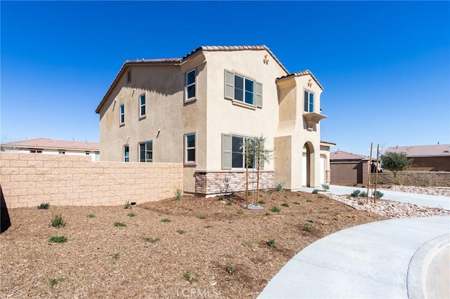 view of front of home featuring stone siding, fence, a tiled roof, and stucco siding