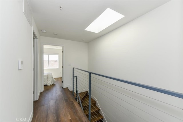 hall with a skylight, baseboards, an upstairs landing, and wood finished floors