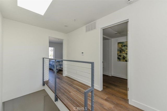 corridor featuring a skylight, visible vents, an upstairs landing, wood finished floors, and baseboards