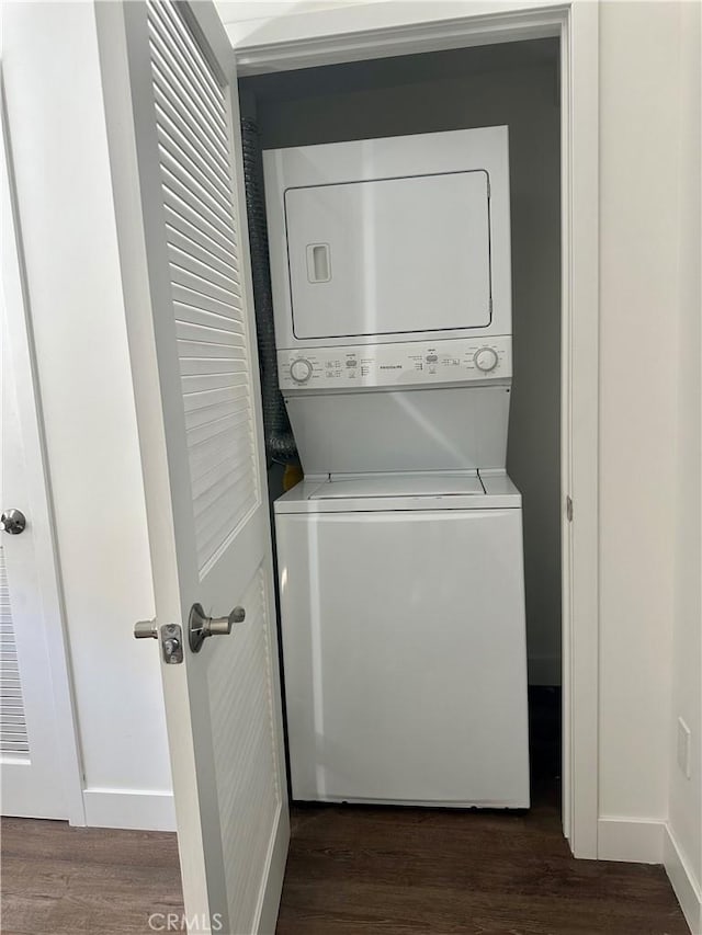 washroom with dark wood-type flooring, laundry area, baseboards, and stacked washing maching and dryer