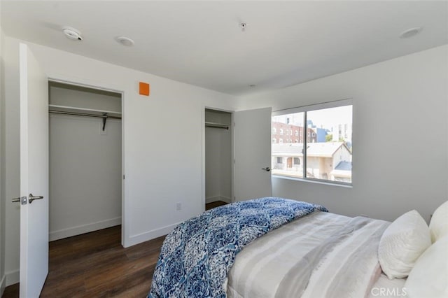 bedroom with baseboards, two closets, and wood finished floors