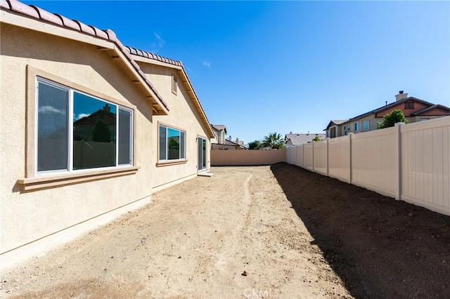 view of side of home with a tile roof, a fenced backyard, and stucco siding