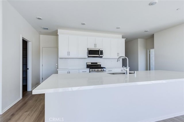 kitchen featuring light wood finished floors, stainless steel appliances, a spacious island, visible vents, and a sink