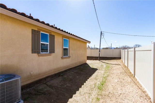 view of side of property with stucco siding, a fenced backyard, and central AC unit