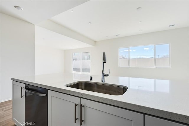 kitchen with light stone counters, light wood-style flooring, white cabinetry, a sink, and dishwashing machine