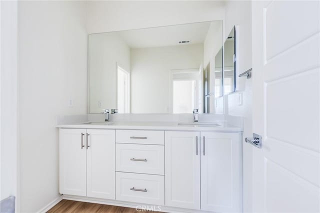 full bathroom with double vanity, visible vents, a sink, and wood finished floors