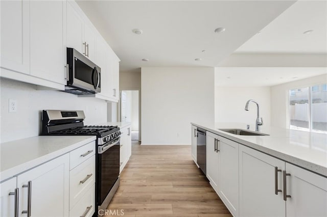 kitchen featuring stainless steel appliances, a sink, white cabinets, light wood-style floors, and light countertops