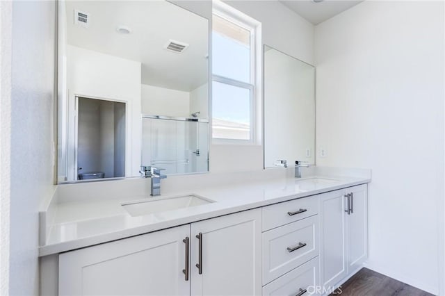 bathroom with double vanity, wood finished floors, a stall shower, and a sink