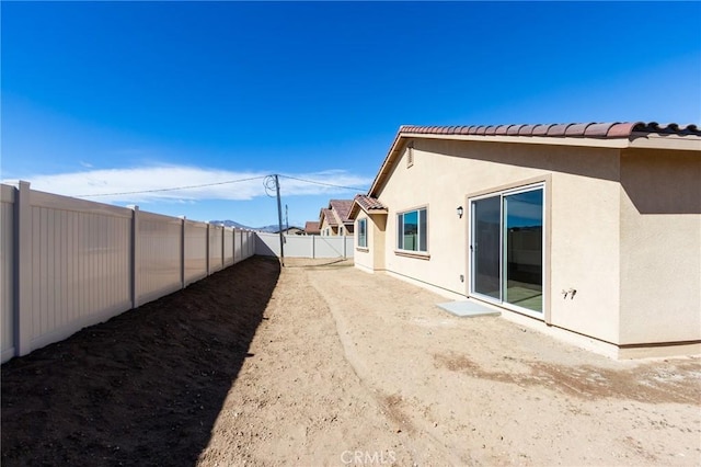 back of house with a fenced backyard, a tiled roof, and stucco siding