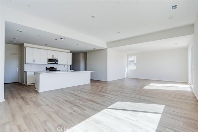 kitchen with visible vents, white cabinets, open floor plan, appliances with stainless steel finishes, and light wood finished floors