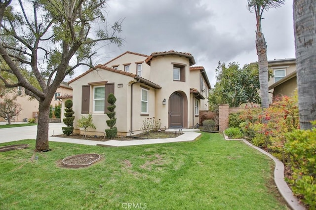 mediterranean / spanish house with a tiled roof, a front yard, and stucco siding