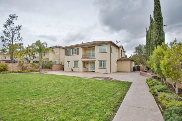 rear view of property with a patio, a lawn, a balcony, and stucco siding