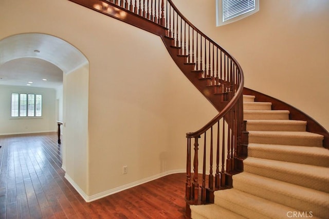 staircase featuring baseboards, arched walkways, and wood finished floors