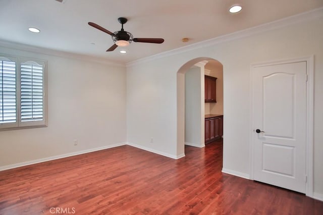 empty room featuring arched walkways, ornamental molding, dark wood-type flooring, and baseboards