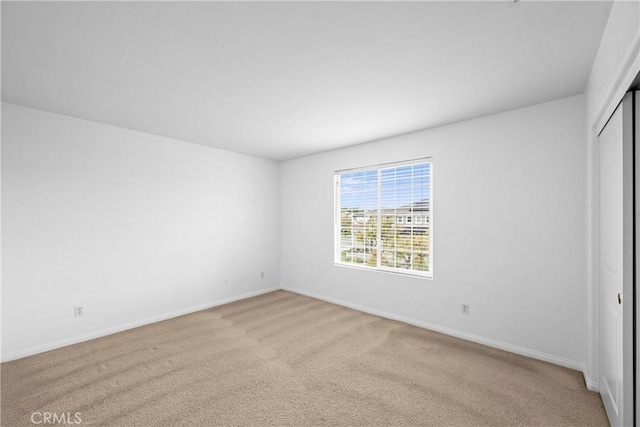 unfurnished bedroom with a closet, light colored carpet, and baseboards