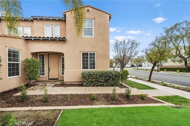 mediterranean / spanish home with a front yard, a tile roof, and stucco siding