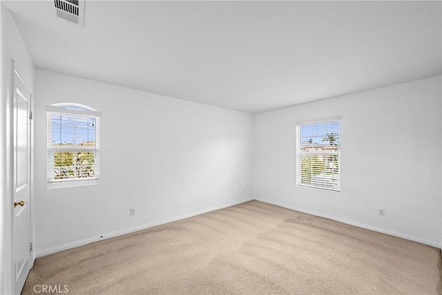 carpeted spare room featuring a wealth of natural light, visible vents, and baseboards