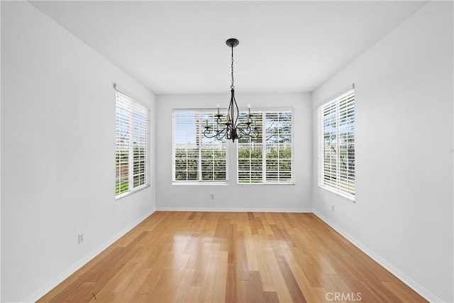 unfurnished dining area featuring light wood-type flooring, an inviting chandelier, and baseboards