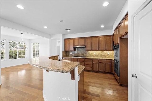 kitchen with tasteful backsplash, under cabinet range hood, black cooktop, and brown cabinets