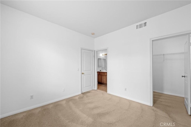 unfurnished bedroom with a walk in closet, visible vents, light carpet, and baseboards