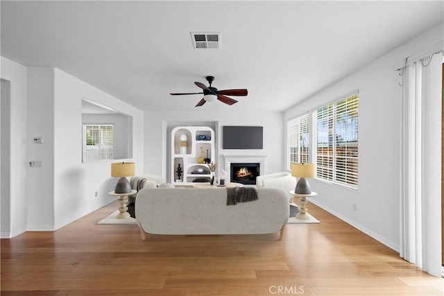 living area with ceiling fan, a lit fireplace, light wood finished floors, and visible vents