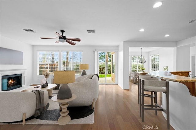 living room featuring light wood-type flooring, visible vents, a glass covered fireplace, and recessed lighting