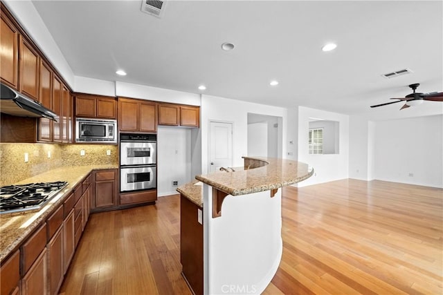 kitchen featuring tasteful backsplash, visible vents, light stone counters, appliances with stainless steel finishes, and wood finished floors