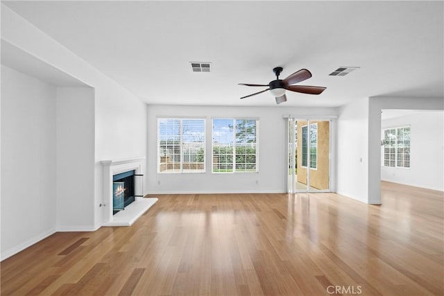 unfurnished living room with plenty of natural light, light wood-type flooring, a glass covered fireplace, and visible vents