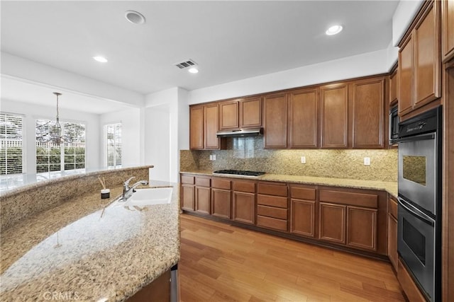 kitchen featuring black gas cooktop, stainless steel double oven, under cabinet range hood, light wood-type flooring, and tasteful backsplash