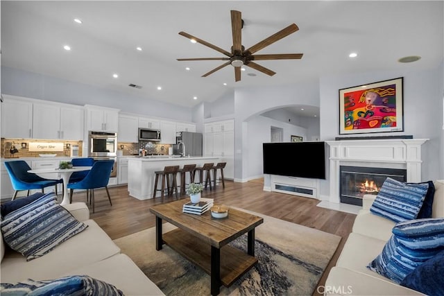 living area with light wood-style floors, a glass covered fireplace, high vaulted ceiling, and recessed lighting