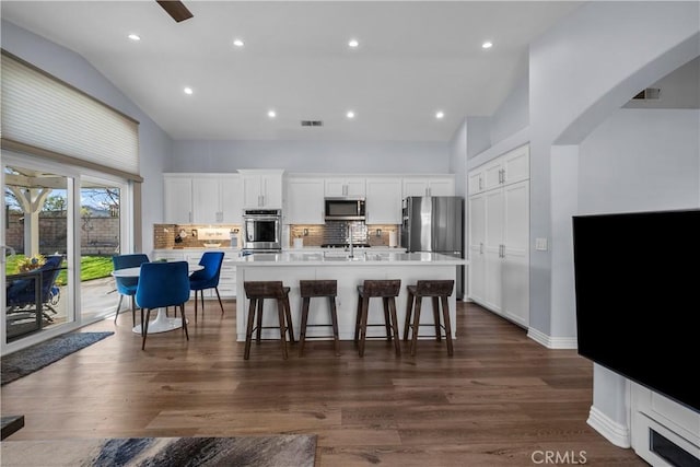 kitchen with a breakfast bar, stainless steel appliances, backsplash, a kitchen island with sink, and high vaulted ceiling